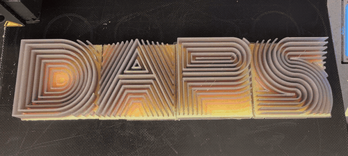 A multicolor 3D-printed sign reading DAPS on a 3D printer bed